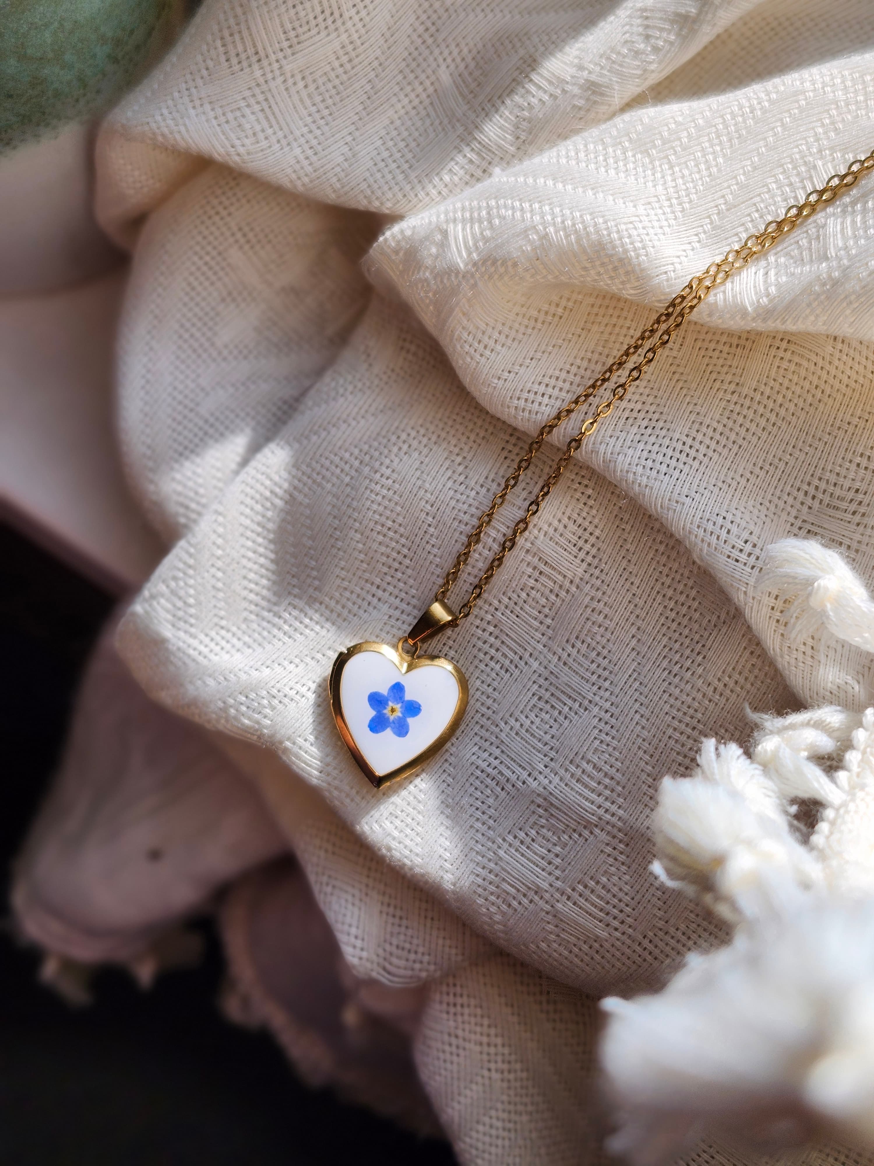 Open heart gold locket holding a blue forget-me-not and tiny white flowers